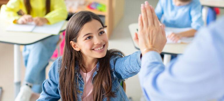 Niña chocando la mano con un docente